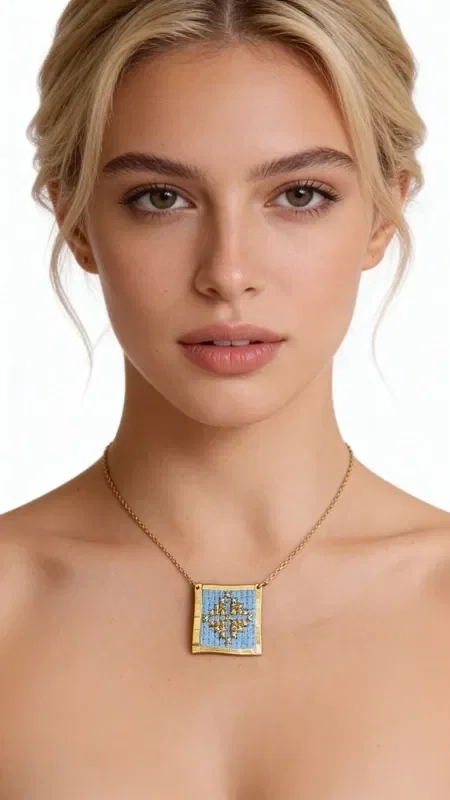 This exceptional embroidered necklace in light blue with geometric patterns is a unique combination of traditional craftsmanship and contemporary design. Designed by Greek Jewelry Designer Aikaterini Chalkiadaki, every detail is hand-embroidered with gold thread on a light blue fabric background, creating a truly distinctive piece of jewelry.

The square embroidered motif features colorful geometric patterns inspired by Greek folklore, while the gold-toned brass frame adds elegance and durability. The delicate gold chain makes this necklace ideal for both everyday and evening looks.

This statement necklace pairs perfectly with monochrome outfits, adding color and character to your look. Handmade construction and quality materials guarantee the longevity of the piece.

Store the necklace in a dry place and clean gently with a soft cloth to preserve the vivid colors of the embroidery.