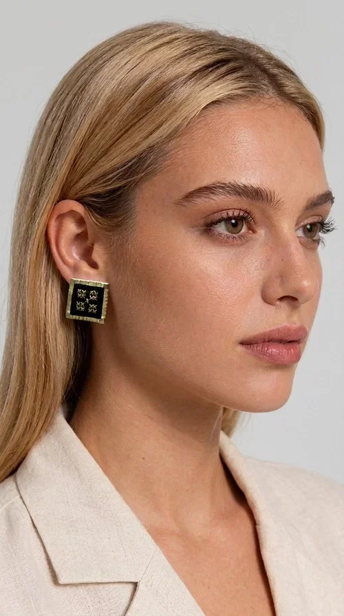 The embroidered statement earrings with geometric patterns in black are the ideal choice for every woman who wants to express her uniqueness through her accessories. Featuring a square shape, a gold-toned brass frame and embroidered floral motifs on black fabric, these handmade earrings combine the traditional art of embroidery with a modern, striking result. Designed by Greek Jewelry Designer Aikaterini Chalkiadaki, they reflect Greek handcraft tradition with a contemporary touch.

The square brass structure with a gold hue perfectly frames the embroidered piece of fabric, where four symmetrical floral motifs in gold stand out, giving a folklore aesthetic with a bold, statement character. These stud earrings suit both casual and formal looks equally well — from an everyday outfit to a wedding or an evening out.