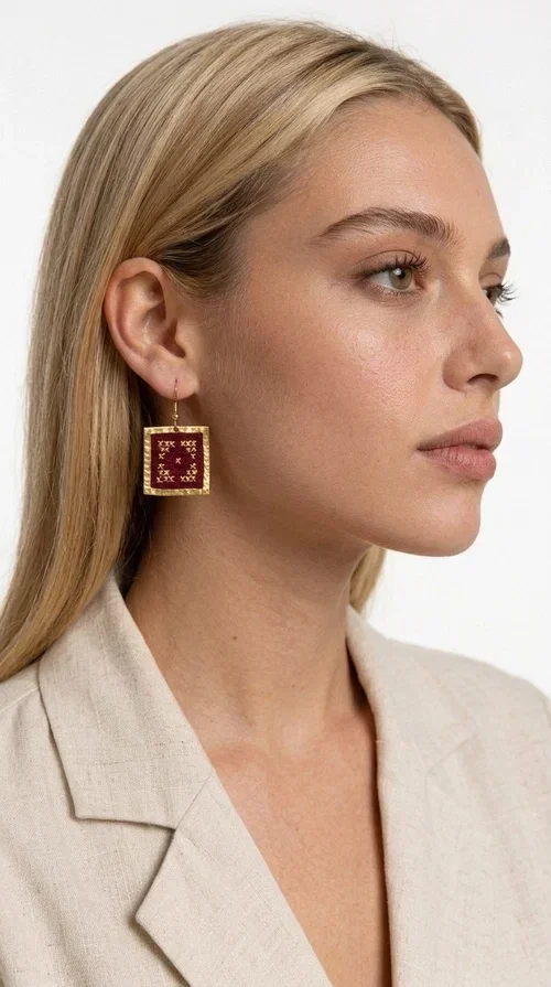 These embroidered statement earrings in deep burgundy are the perfect choice for those seeking jewelry with character, combining the traditional art of embroidery with contemporary aesthetics.

Designed by Greek Jewelry Designer Aikaterini Chalkiadaki, these handmade earrings feature a square brass frame in gold tone, with a finely detailed embossed surface that highlights their premium quality. Inside, deep red fabric in a burgundy shade is adorned with geometric cross-stitch embroidery designs — a nod to folk tradition that takes on a modern, urban character.

These dangle earrings pair equally well with casual and formal outfits, from everyday looks to appearances at weddings, christenings, or corporate events. Their burgundy color makes them ideal for autumn and winter looks, while their statement aesthetic guarantees they won't go unnoticed.
