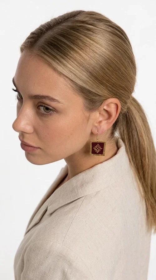 Embroidered statement earrings in deep burgundy are the ideal choice for every woman looking for jewelry with character and a unique aesthetic. With a square shape and delicate geometric embroidered details in gold, they combine the traditional art of embroidery with a completely modern result — creating a piece of jewelry that stands out.

Designed by Greek Jewelry Designer Aikaterini Chalkiadaki, these handmade earrings are crafted from brass and embroidered fabric, achieving a beautiful combination of materials that evokes a folk aesthetic. The geometric motifs on the embroidered section exude folklore charm, while the golden brass metal frame gives structure and balance to the overall design.

The burgundy embroidered dangle earrings are perfect for evening and formal occasions, such as weddings, christenings and festive events, while also instantly elevating a casual look. The rich burgundy tone makes them especially flattering for all skin tones.