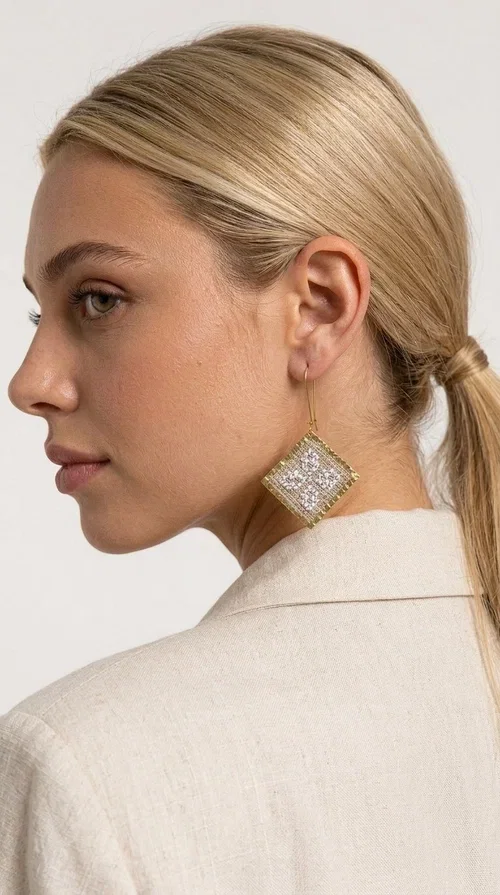 The embroidered statement earrings with geometric patterns in cream are a bold choice for every woman who loves handmade aesthetics with folk inspiration. Designed by Greek Jewelry Designer Aikaterini Chalkiadaki, these earrings combine the traditional art of embroidery with modern design, creating a truly standout result.

The square-diamond shape with its bold geometric structure and rich embroidered motifs in a cream shade gives off a vintage, elegant feel. The gold-tone brass framing the fabric adds warmth and shine, while the dangling design through a gold-tone hoop ensures comfortable wear. Ideal for weddings, christenings, festive events, and also for casual boho looks that call for a strong statement piece.