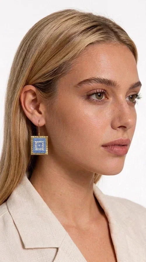 The embroidered statement earrings with geometric patterns in light blue are the ideal choice for every woman who wants to express herself through fashion in a unique, handmade way. Designed by Greek Jewelry Designer Aikaterini Chalkiadaki, these striking dangle earrings combine the traditional art of embroidery with contemporary design, creating a piece of jewelry that stands out instantly.

Made of brass with a gold finish and fabric in shades of light blue, these earrings feature geometric motifs inspired by Greek folk art and folklore tradition. Their square shape with concentric embroidered patterns gives them a distinctive boho-ethnic character that suits both everyday outfits and more formal looks — from a summer party to a wedding or christening.
