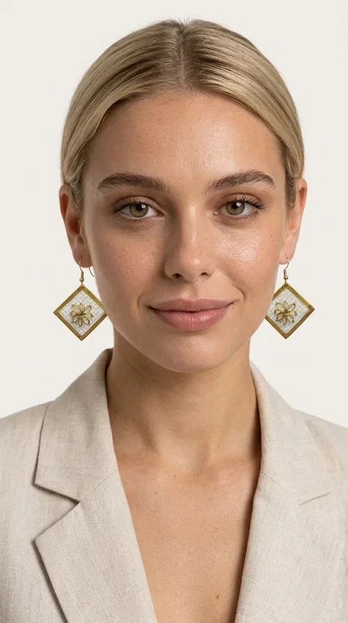 The embroidered statement earrings with geometric patterns in white and gold are the perfect choice for those seeking a piece of jewelry that combines folk art with contemporary design. Designed by Greek Jewelry Designer Aikaterini Chalkiadaki, these handmade dangle earrings impress with their geometric diamond shape and the embroidered floral decoration at their center.

Made of brass and fabric, they feature a gold frame surrounding a white embroidered section with a raised floral motif — a detail that evokes traditional Greek embroidery art. They hang from a gold hoop, creating an elegant yet striking result. Ideal as earrings for a wedding, christening or any formal event, but also as a boho statement piece for casual looks.