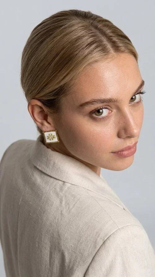 Embroidered statement earrings with geometric designs in white are the perfect choice for those seeking an accessory that combines folk tradition with contemporary style. Designed by Greek Jewelry Designer Aikaterini Chalkiadaki, these handmade stud earrings are a unique piece that stands out with its embroidered technique and geometric folk-inspired patterns.

Made of brass and fabric, these earrings feature a square shape with white embroidery and gold geometric details reminiscent of folklore tradition. The white color makes them versatile and easy to pair with any outfit — from casual everyday looks to formal occasions, weddings, and christenings. Their lightweight design ensures comfort throughout the day.

Ideal for women who love striking jewelry with character, these boho earrings flatter every face shape thanks to their structured form. Perfect as a gift for any occasion.