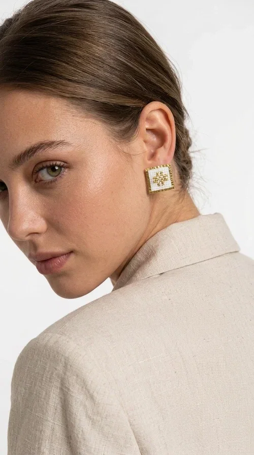 The embroidered statement earrings with geometric patterns in white are the ideal choice for anyone who wants to express their unique personality through a piece of jewelry with character and soul. Designed by Greek Jewelry Designer Aikaterini Chalkiadaki, these handmade stud earrings combine the traditional art of embroidery with modern aesthetics, creating a result that truly stands out.

Each pair has a square shape and is decorated with a carefully embroidered geometric motif on white fabric, with gold details that highlight the design and add shine. The gold-toned brass frame completes the look harmoniously, while the raised texture of the embroidery adds depth and distinctive character. These are statement pieces that move between folklore and contemporary style.

Ideal for wedding ceremonies, formal occasions, or to elevate a casual outfit, these striking earrings pair equally well with a linen blazer, an evening dress, or a boho ensemble. Thanks to the combination of white and gold, they match almost any color palette.