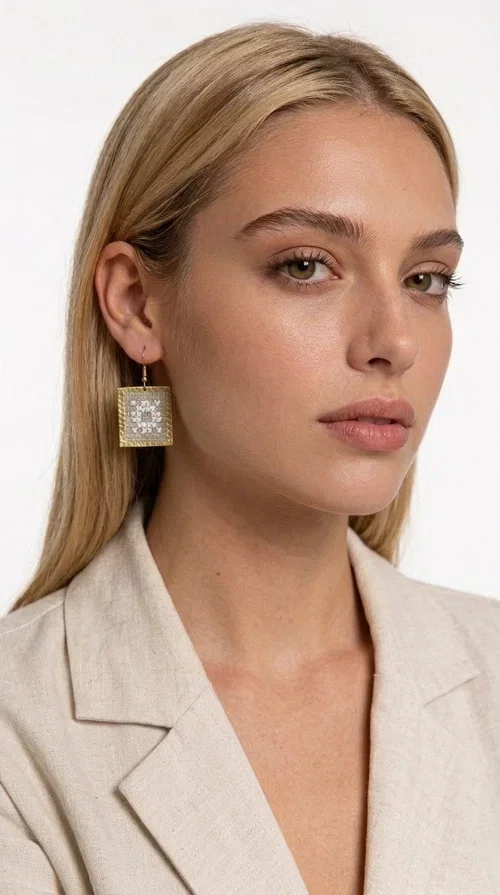 Embroidered statement earrings with geometric patterns in a cream shade are the ideal choice for anyone seeking an accessory that combines the traditional art of embroidery with a modern, eye-catching aesthetic.

Designed by Greek Jewelry Designer Aikaterini Chalkiadaki, these handmade earrings are a unique combination of brass and fabric. Their square shape in a golden hue elegantly frames the embroidered geometric motif at the center, inspired by Greek folk art and tradition. The warm cream tone of the embroidery exudes a timeless elegance that suits both casual and formal looks equally well.

These striking dangle earrings instantly elevate any outfit — from a simple linen jacket to an evening dress for a wedding or christening. They make a perfect gift for women who appreciate craftsmanship and distinctive design.