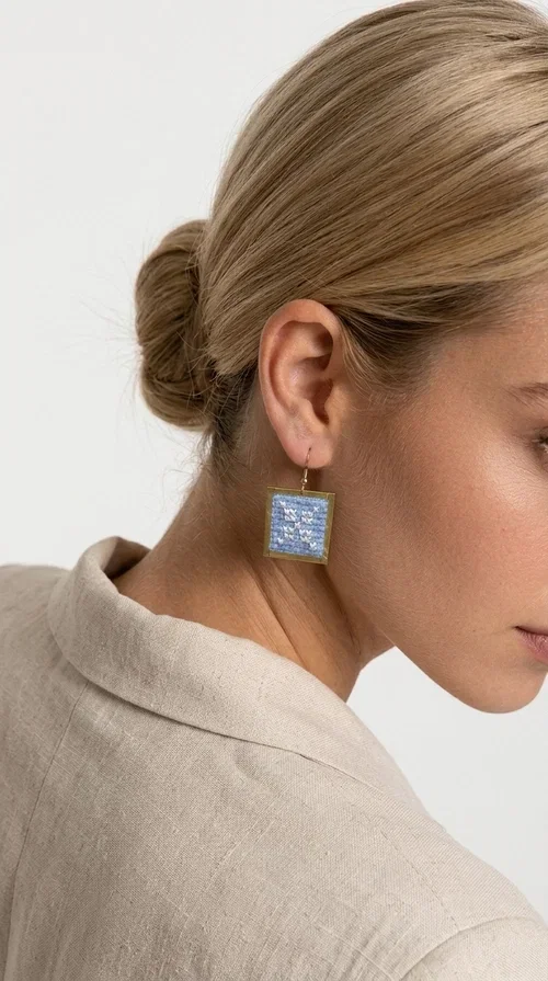 Embroidered statement earrings in light blue are the ideal choice for anyone who wants to add a touch of color and personality to their everyday or evening look. With a square shape and geometric embroidered motifs inspired by folk tradition, these earrings combine a handmade aesthetic with a modern, boho-folk style. Designed by Greek Jewelry Designer Aikaterini Chalkiadaki, they are a unique piece that carries the soul of Greek craftsmanship.

Made from brass and fabric, the earrings feature a golden metallic frame surrounding a light blue embroidered panel with white geometric details. The combination of materials creates a lightweight piece that is comfortable to wear, even after hours of use. Their square shape and folklore motif make them ideal for women looking for striking earrings with character.

They pair beautifully with casual summer looks, linen outfits, boho dresses, as well as more formal appearances at weddings or christenings. The light blue palette makes them perfect for spring and summer, while their geometric motifs also make them suitable for winter events.