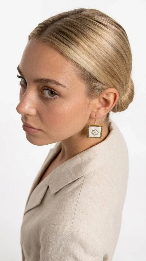 Embroidered statement earrings with geometric patterns in white are a bold choice for every woman who loves handmade jewelry with character and style. Designed by Greek Jewelry Designer Aikaterini Chalkiadaki, these striking earrings combine the traditional art of embroidery with a modern, geometric aesthetic that stands out.

Made from brass and fabric, the earrings feature a square shape with a gold-toned brass metal frame surrounding a finely embroidered white center adorned with floral and geometric motifs. The result is an accessory that evokes Greek folk tradition while fitting seamlessly into a modern, everyday or festive style.

Ideal for weddings, christenings, nights out, or even to elevate a simple office look, these earrings pair beautifully with linen, boho, or minimal outfits. The white palette makes them versatile and timeless.