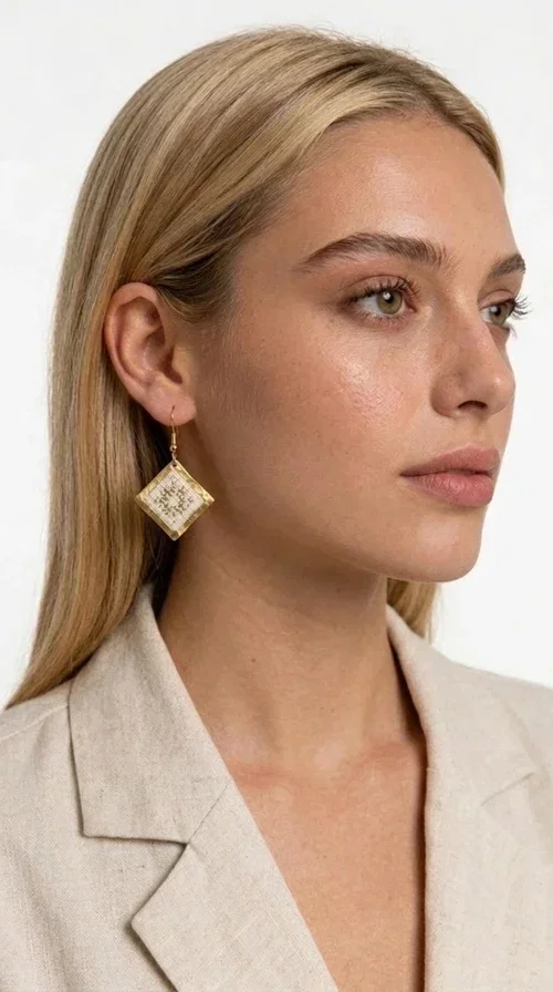 Embroidered statement earrings with geometric patterns are the ideal choice for every woman who wants to add a folk-chic touch to her look. Designed by Greek Jewelry Designer Aikaterini Chalkiadaki, these handmade earrings combine the tradition of embroidery art with a modern, geometric aesthetic that stands out.

Their diamond shape in white fabric with gold embroidery details and a gold brass frame creates a result that is both elegant and striking. They hang lightly from a gold hook, gently touching the neck and adding movement with every step. Ideal for both everyday wear and special occasions, they pair beautifully with linen and boho outfits, summer dresses, as well as casual-chic looks all year round.