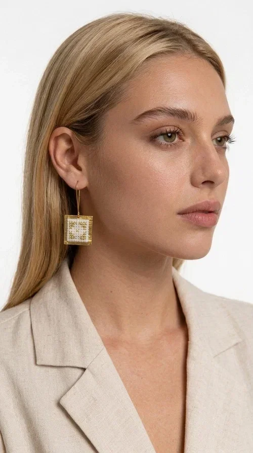 Embroidered statement earrings with geometric designs are the ideal choice for those seeking an accessory that combines the traditional art of embroidery with contemporary design. Designed by Greek Jewelry Designer Aikaterini Chalkiadaki, these handmade earrings bring Greek aesthetics to the forefront in a bold and modern way.

Each pair features a square embroidered pendant in white with gold geometric details reminiscent of folk-inspired aesthetics. The gold-tone brass frame gives structure and elegance to the piece, while the hook clasp ensures comfortable and secure wear. The result is a piece of jewelry that immediately draws attention without being heavy or bulky.

Ideal for weddings, christenings, festive events, or even to elevate an everyday casual outfit, these particular drop earrings pair equally well with dresses, blazers, and boho-style looks.