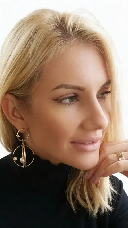 Discover the magic of three-dimensional statement earrings that highlight your femininity in a striking way. These unique handmade dangle hoop earrings, crafted from brass and designed by Greek Jewelry Designer Aikaterini Chalkiadaki, combine modern aesthetics with the classic elegance of pearls.

The innovative geometric design features a system of gold-tone hoops that create a stunning visual effect, while the natural pearls add a touch of luxury. Each earring has two layers of hoops connected by a vertical bar, creating a three-dimensional structure ideal for those who love eye-catching accessories.

These large earrings are the perfect choice for bridal looks, evening outings, or any moment you want to stand out. The golden hue of the brass suits all skin tones and pairs easily with any style of dressing.