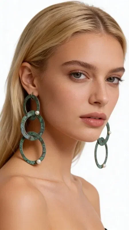 Discover the magic of large statement earrings that combine the elegance of copper with a green patina in a truly unique design. These handmade long stud earrings, designed by Greek Jewelry Designer Aikaterini Chalkiadaki, create a statement look that catches every eye.

The innovative design with interlocking rings in green patina gives a bohemian aesthetic that suits modern women perfectly. Each ring is handcrafted from high-quality copper and adorned with natural pearls that add shine and elegance. The unique green patina creates a vintage feel that blends seamlessly with both modern and classic outfits.

These dangling earrings are ideal for special occasions, bridal looks, or everyday chic outfits. Greek craftsmanship shows in every detail, from the perfect balance of the rings to the careful placement of the pearls. Store them in a dry place and clean gently with a soft cloth.