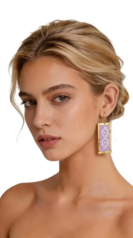 Statement earrings featuring embroidered geometric designs in gold thread on a lilac background are the perfect choice for women who love striking and original jewelry. Designed by Greek Jewelry Designer Aikaterini Chalkiadaki, these handmade earrings combine the traditional art of embroidery with contemporary design.

Each earring is crafted with special attention to detail, using gold thread that forms beautiful geometric patterns in a soft lilac hue. Their rectangular shape and dangling style make them ideal for every occasion, from everyday outfits to special appearances and wedding events.

These embroidered earrings offer a unique sense of elegance and style, while their lightweight construction ensures comfortable wear all day long. Their folklore-inspired design reflects Greek tradition in a modern style.

Material: Brass, Fabric

Handle gently with a dry cloth and store in a safe place to preserve their beauty.