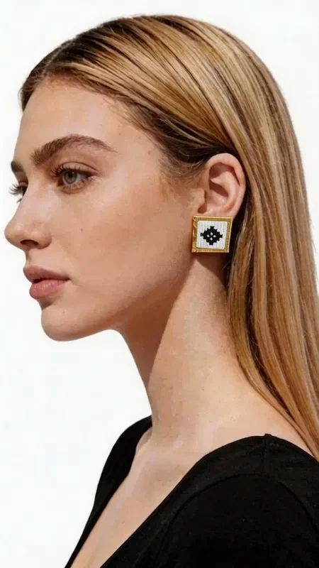 Stand out with these striking statement earrings, embroidered with geometric patterns in white, combining the traditional art of goldwork embroidery with contemporary design. Designed by Greek Jewelry Designer Aikaterini Chalkiadaki, these handmade earrings are the perfect choice for any woman who wants to express her personality with style.

The embroidered geometric motif in white and black creates a striking visual contrast that catches every eye. The gold-tone base adds luxury and elegance, while their square shape makes them ideal for modern looks. These statement earrings pair perfectly with professional outfits, casual looks, or wedding ceremonies.

Material: Brass, Fabric

Care for your earrings by storing them in a dry place and cleaning them gently with a soft cloth. Avoid contact with perfumes and moisture to preserve their beauty for years to come.