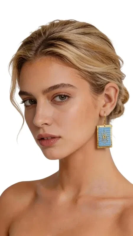 The statement embroidered earrings with geometric patterns in gold thread on light blue are a unique combination of traditional craftsmanship and modern design. Designed by Greek Jewelry Designer Aikaterini Chalkiadaki, these striking handmade earrings enhance the elegance of any look with style and character. The delicate embroidery technique with gold thread creates a beautiful effect that subtly shimmers, while the light blue color offers a freshness that pairs perfectly with spring and summer outfits. The geometric patterns give a modern aesthetic, making these striking earrings an ideal choice for any occasion. The handmade embroidered earrings are perfect for weddings, christenings, summer parties and every special moment where you want to stand out. Pair them with white or blue clothing to highlight their light blue color. Material: Brass, Fabric. Take care of your earrings by storing them in a dry place, away from moisture and direct sunlight, to preserve their shine.