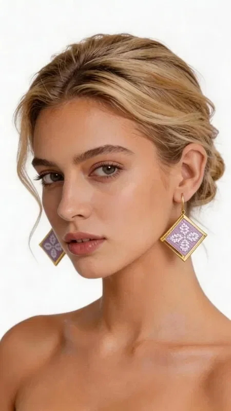 , These statement embroidered earrings in a soft lilac shade with geometric patterns in gold thread are the perfect choice for adding a touch of elegance and originality to your look. Designed by Greek Jewelry Designer Aikaterini Chalkiadaki, these handmade earrings combine the traditional technique of embroidery with contemporary design. Their square geometric shape is adorned with intricately embroidered motifs in a soft lilac tone, while the gold outline adds a luxurious touch. The folklore design with its detailed geometric patterns creates a unique piece of jewelry that stands out and complements both casual and formal looks. Ideal for women who love statement accessories, these earrings are perfect for special occasions, weddings, or for adding a splash of color to your everyday style.

Material: Brass, Fabric. To care for them, store the earrings in a dry place and avoid contact with water and chemicals.