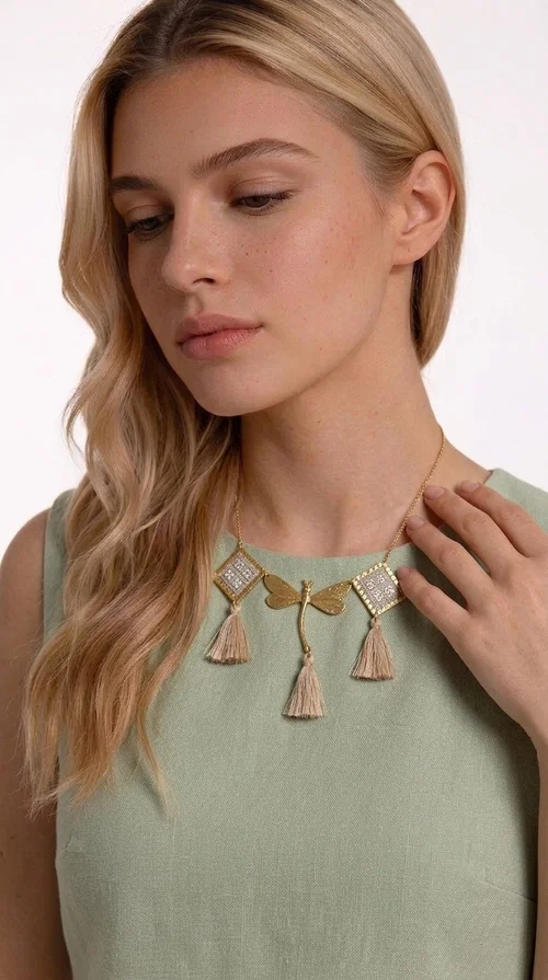 The statement embroidered ivory necklace with geometric designs is a handmade piece that combines the traditional art of embroidery with a modern aesthetic, creating a result that instantly catches the eye. Designed by Greek Jewelry Designer Aikaterini Chalkiadaki, it is a tribute to folk art and Greek craftsmanship.

The necklace features gold-toned geometric brass elements in a diamond shape, adorned with delicate embroidered motifs in an ivory hue, evoking the rich aesthetic vocabulary of folklore. Among them, a gold metallic dragonfly-shaped element adds grace and movement to the piece. Three fabric tassels in an ivory-beige shade hang elegantly, giving depth and motion to the jewelry.

Ideal for summer outfits, boho and ethnic looks, as well as for elevating a simple dress or blouse. It pairs perfectly with linen clothing, maxi dresses, or casual summer looks.