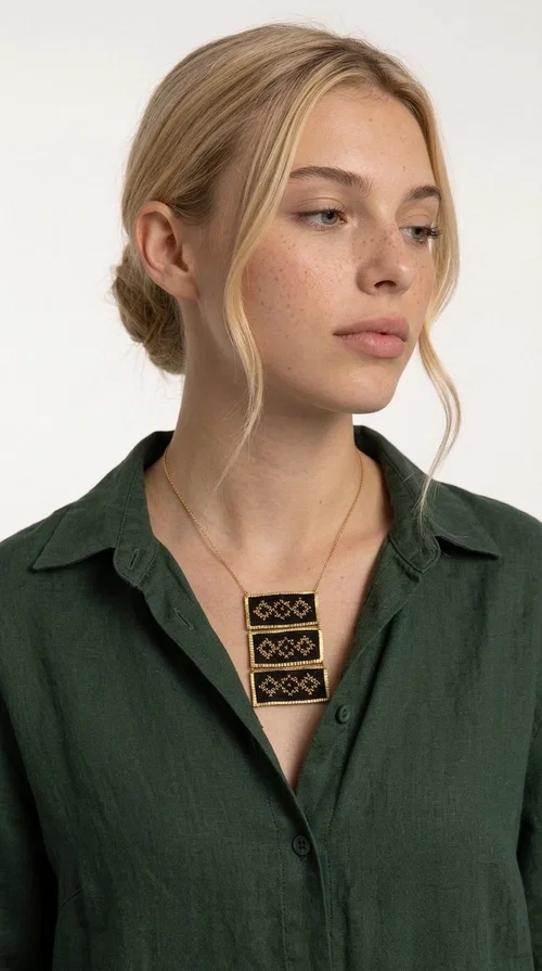 An embroidered necklace that combines traditional Greek aesthetics with modern fashion — the Statement necklace KOL-4774 is a handmade creation that instantly catches the eye.

Designed by Greek Jewelry Designer Aikaterini Chalkiadaki, this necklace features three rectangular fabric plaques in deep black, adorned with gold-toned embroidered geometric designs inspired by Greek folk tradition. The frame of each plaque, made of gold-toned brass, gives the piece a rich, striking presence. The accompanying brass chain keeps the composition light on the neck, while the overall look exudes a unique blend of ethnic and contemporary style.

Ideal for women who love statement jewelry and want to elevate simple outfits — a linen shirt, a black dress, or even a casual look — with a wonderful touch of individuality. Perfect for nights out, events, weddings, or everyday wear when you want to stand out.
