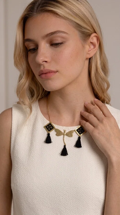 A statement embroidered necklace that instantly catches the eye — the perfect piece for every woman who wants to express herself with style and personality. Designed by Greek Jewelry Designer Aikaterini Chalkiadaki, this unique necklace combines the traditional art of embroidery with a modern, striking result. Its geometric composition and bold black palette make it a timeless statement piece that truly stands out.

The necklace features three square brass motifs with black embroidered geometric patterns, inspired by folk aesthetics. At the center sits a striking gold-tone metal element shaped like a dragonfly or butterfly, while elegant black fabric tassels hang from each motif, adding movement and lightness. The chain is gold-toned brass, durable and lightweight to wear.

Ideal for daytime looks with white or monochrome outfits, as well as for evening occasions that call for character. It pairs perfectly with simple dresses, tailored outfits, and casual looks.
