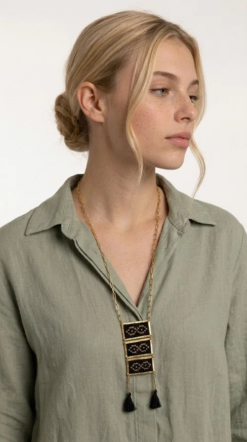 An embroidered necklace that blends tradition with contemporary style — the Statement Necklace KOL-4754 is the perfect choice for any woman who wants to express herself through her jewelry. Designed by Greek Jewelry Designer Aikaterini Chalkiadaki, this handmade necklace features geometric embroidered patterns inspired by Greek folk tradition, creating a unique piece full of character.

Three rectangular brass frames in a gold hue are adorned with black embroidery in geometric motifs, while black tassels at the bottom add movement and dramatic flair. The gold paperclip-style chain completes the look with an elegant, modern touch. The result is a striking long necklace that suits both everyday and evening outfits equally well.

Wear it over a simple shirt or dress to create a look full of personality. It's the perfect gift choice, and also the perfect way to turn heads at an evening event.