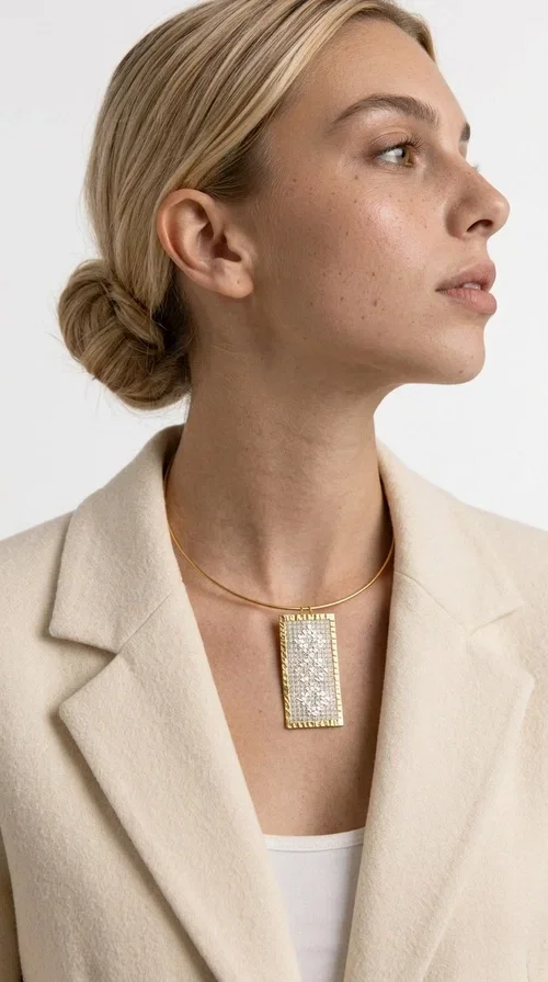 A statement embroidered necklace that instantly catches the eye — featuring geometric patterns in cream tones and an aesthetic that blends folk tradition with contemporary style. Designed by Greek Jewelry Designer Aikaterini Chalkiadaki, this handmade piece is a distinctive choice for those seeking something beyond the ordinary.

The rectangular embroidered pendant in cream-gold tones is crafted from brass and fabric, featuring dense embroidery in geometric motifs reminiscent of folklore aesthetics. It hangs from a delicate gold-toned choker-torque style chain that elegantly and strikingly highlights the neckline. The extensive decoration with small shimmering elements adds richness and depth to the overall composition.

Ideal for casual chic or smart casual looks, it pairs beautifully with a white T-shirt, a blazer, or a summer dress. It also makes an excellent gift idea for women who appreciate handmade jewelry with a distinctive character.