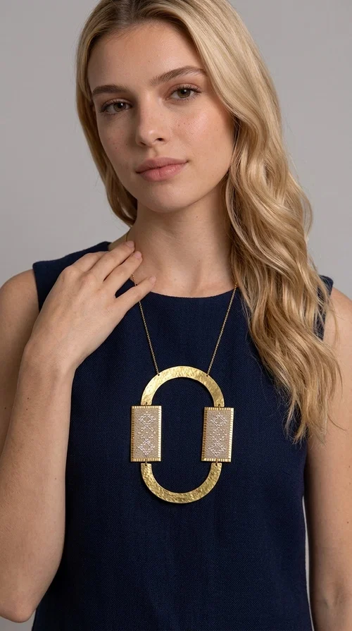 A statement embroidered necklace that instantly catches the eye — featuring geometric patterns in an ecru shade combined with gold-toned brass that highlights its uniqueness. Designed by Greek Jewelry Designer Aikaterini Chalkiadaki, this handmade necklace blends the tradition of embroidery art with a modern, striking aesthetic result.

The ecru-colored embroidered fabric is set within two rectangular gold-toned brass frames, connected through a large oval element — creating a geometric composition full of character. The necklace hangs from a delicate gold chain, positioning the pendant right at the center of the chest for maximum visual impact. Ideal as a long statement necklace for casual or formal looks.

It pairs perfectly with simple dresses, pant-and-top sets, or low-cut tops that let the jewelry speak for itself. A perfect gift for loved ones who appreciate handmade, one-of-a-kind jewelry.