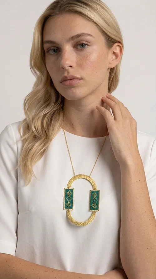 A statement embroidered necklace that turns every look into a style declaration — featuring geometric patterns inspired by Greek folk tradition and an aesthetic that speaks for itself.

Designed by Greek Jewelry Designer Aikaterini Chalkiadaki, this long necklace combines brass and fabric in a handmade composition that highlights the art of embroidery. The oval golden brass frame embraces two rectangular fabric elements in deep green, adorned with gold-toned geometric motifs reminiscent of traditional embroidery techniques. The result is a jewelry piece with strong character, blending tradition with contemporary aesthetics.

Ideal for women who love striking jewelry, this long green necklace pairs perfectly with simple outfits — a white t-shirt, a solid-color dress, or a chic blazer. It instantly adds color, geometry, and personality to any ensemble, summer and winter alike.