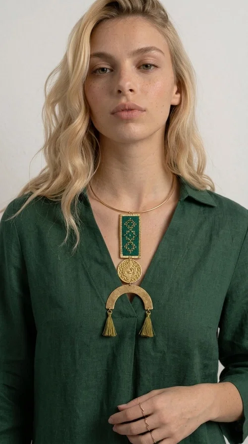 A statement embroidered necklace that instantly catches the eye — featuring a bold green color, geometric patterns and gold details reminiscent of the tradition of folk jewelry.

Designed by Greek Jewelry Designer Aikaterini Chalkiadaki, this handmade necklace combines brass and fabric in a composition that highlights the skill of Greek craftsmanship. The rectangular embroidered piece, with its delicate geometric motifs in gold and green tones, blends harmoniously with a gold circular disc and a brass arc, while three hanging tassels in a khaki-gold shade add movement and warmth to the overall look. It is worn on a gold rigid choker for an even more striking effect.

Ideal for looks that want to stand out — from summer evening outings to casual chic styles with simple linen or cotton clothing. It pairs perfectly with neutral tones, white, ecru, or deep green shades.