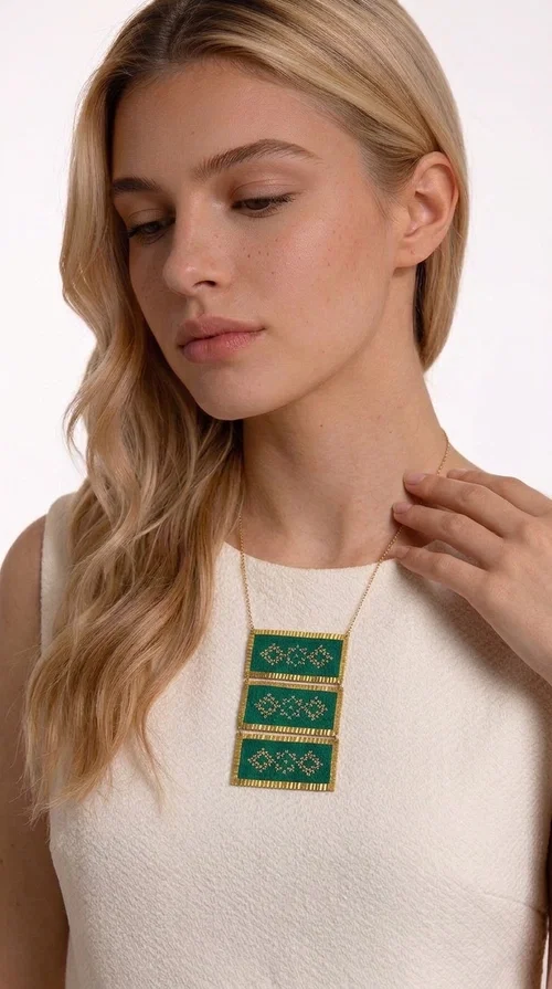 An embroidered green necklace that blends tradition with contemporary design — ideal for those who want to make a statement in a truly unique way. Designed by Greek Jewelry Designer Aikaterini Chalkiadaki, this striking necklace brings a breath of fresh air to the world of handmade jewelry. The deep green fabric combined with golden geometric embroidered motifs creates a sense of richness and authenticity rarely found in mass-produced jewelry.

The necklace is made of three rectangular brass sections, covered in green fabric and adorned with embroidered geometric patterns inspired by Greek folk tradition (folklore). The delicate gold chain that accompanies it adds grace and balance, making it ideal for both daytime looks and evening outings. It pairs perfectly with white, ecru, or monochrome outfits, instantly adding character to any look.