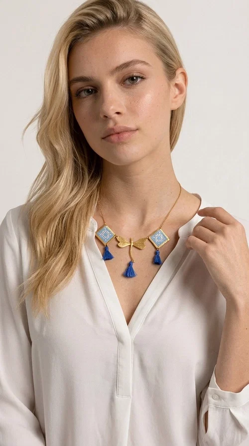 A statement necklace that combines the tradition of embroidery art with contemporary aesthetics — ideal for those who want to stand out with style and character.

Designed by Greek Jewelry Designer Aikaterini Chalkiadaki, this handmade embroidered necklace in light blue brings to the forefront the magic of geometric patterns inspired by Greek folk tradition. Fabric rhombuses with finely worked embroidery in light blue and white shades alternate with a golden dragonfly made of brass, while four hanging tassels in deep blue add movement and vibrancy to the composition. The golden brass chain completes a creation full of color, texture and atmosphere.

Wear it over a white shirt or a simple monochrome dress to highlight all its beauty. It fits perfectly with summer looks, romantic evening outings, and boho-chic day looks as well. It is also an excellent gift choice for a woman who loves striking, handmade jewelry.