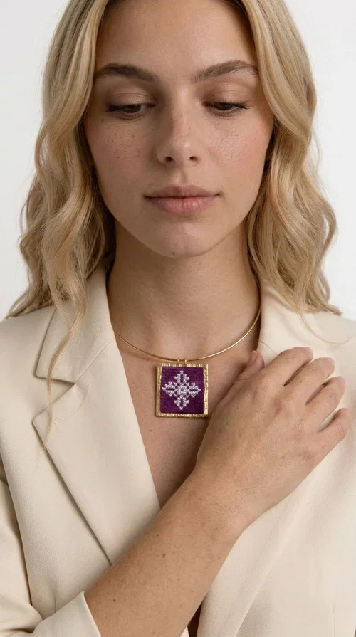 The embroidered magenta necklace with geometric patterns is a statement piece that combines the traditional art of embroidery with a modern aesthetic — ideal for every woman who wants to express herself boldly and stylishly.

Designed by Greek Jewelry Designer Aikaterini Chalkiadaki, this handmade necklace features a square pendant in deep purple-magenta fabric, adorned with a white embroidered geometric design inspired by folk art tradition. The golden brass metal frame elegantly encases the pendant, while the delicate gold choker-style chain showcases it flawlessly around the neck. The result is a piece of jewelry with soul, character, and a strong visual presence.

Wear it over a white shirt, dress, or blazer to create a striking combination. It looks equally great in casual and more formal outfits, making it a versatile accessory for any occasion.