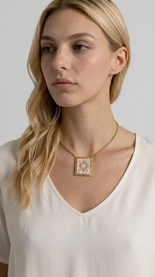 An embroidered necklace that combines the traditional art of embroidery with a modern aesthetic — ideal for every woman who loves statement jewelry with character. Designed by Greek Jewelry Designer Aikaterini Chalkiadaki, this handmade necklace is a unique example of folklore-inspired aesthetics drawing from Greek tradition.

The square pendant in pink and gold tones is adorned with geometric patterns embroidered on fabric, set into a gold-tone brass base with a textured surface. The gold rolo chain gives the piece an elegant, contemporary touch that makes it easy to style — whether with an everyday casual look or an evening outfit.

The pink palette with gold embroidered details offers a warm, feminine feel, while the handmade construction guarantees uniqueness. An ideal gift for women who appreciate jewelry with history and soul.