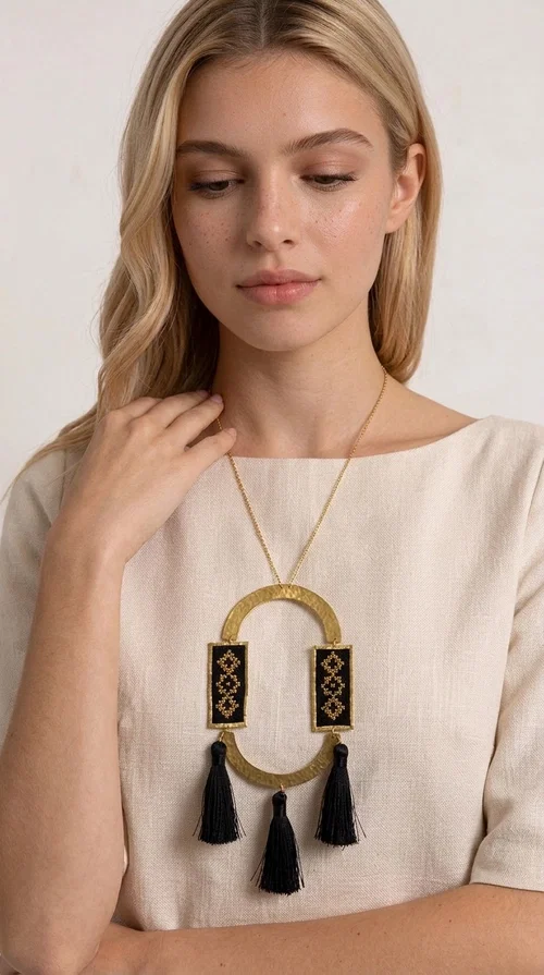 A statement embroidered necklace that blends tradition with modern aesthetics — ideal for every woman who wants to express herself with style and character.

Designed by Greek Jewelry Designer Aikaterini Chalkiadaki, this striking long necklace is an ode to folk art and craftsmanship. Two rectangular embroidered plaques with geometric patterns in black and gold are framed by a golden brass arch, while three black tassels add movement and boho-chic charm. The gold-tone chain completes the composition with an elegant finishing touch.

This embroidered necklace pairs beautifully with simple white or ecru outfits that let the piece take center stage, as well as with evening looks that need that extra touch. Worn alone, it instantly turns any look into a statement.