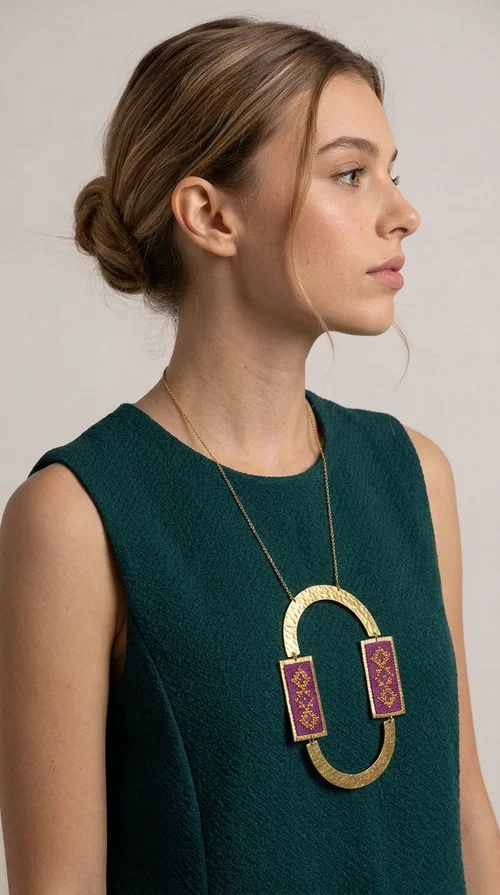 An embroidered necklace that instantly catches the eye — the Statement Necklace KOL-4753 combines the tradition of Greek embroidery art with a modern, geometric aesthetic. Designed by Greek Jewelry Designer Aikaterini Chalkiadaki, this striking long necklace is the ultimate statement piece for every woman who appreciates handmade artistry and uniqueness.

The necklace features two rectangular fabric elements in deep burgundy, adorned with gold embroidery of geometric patterns inspired by folklore aesthetics. The embroidered sections are framed by shiny gold-toned brass, forming a large oval shape — a bold design choice that highlights the uniqueness of the piece. The gold-toned chain offers an elegant long line that pairs perfectly with simple, monochrome outfits.

Ideal for stylish daytime looks as well as evening outings, this necklace suits both casual and formal ensembles equally well. It gives your look an authentic, artistic character.